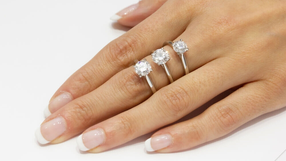 Hand wearing three solitaire diamond engagement rings with different diamond carat size